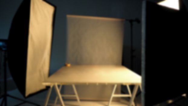 Blurry image behind the scenes of shooting video production in a studio with small set professional lighting equipment.