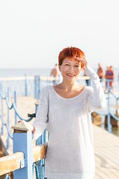 Wide smiling young woman with red short hair cut on clear sky background. Coastal morning. Natural beauty. Happiness and power of youth.