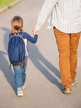 Father takes his son to school. Back to school after summer holidays. Dad and kid walk on street hand in hand. Family time, moral support.