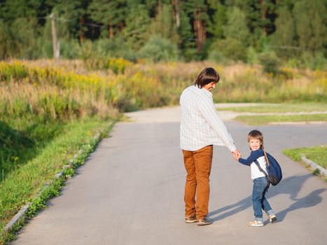 Father takes his son to school. Back to school after summer holidays. Dad and kid walk on street hand in hand. Family time, moral support.