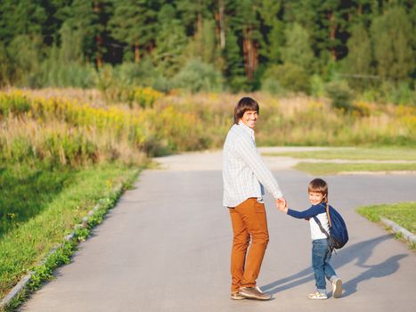 Father takes his son to school. Back to school after summer holidays. Dad and kid walk on street hand in hand. Family time, moral support.