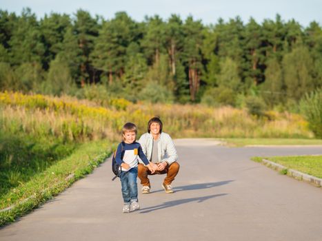 Father takes his son to school. Back to school after summer holidays. Dad and kid walk on street hand in hand. Family time, moral support.