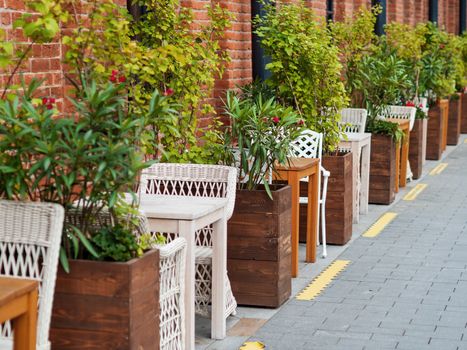 Loft outdoor cafe. Tables and chairs are separate from each other with potted plants and flowers. Social distancing because of coronavirus COVID-19.