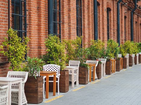 Loft outdoor cafe. Tables and chairs are separate from each other with potted plants and flowers. Social distancing because of coronavirus COVID-19.