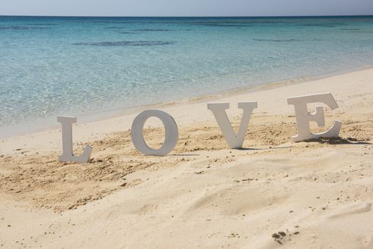 Closeup of romantic love sign on tropical island sandy beach paradise with ocean in background