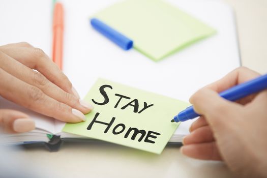 Hands of woman writing on adhesive note with Stay Home text