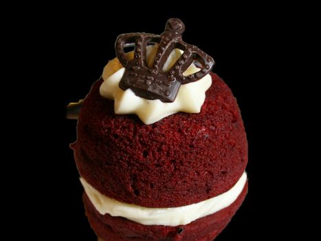 Closeup of a red velvet cake topped with a chocolate crown isolated on black background.