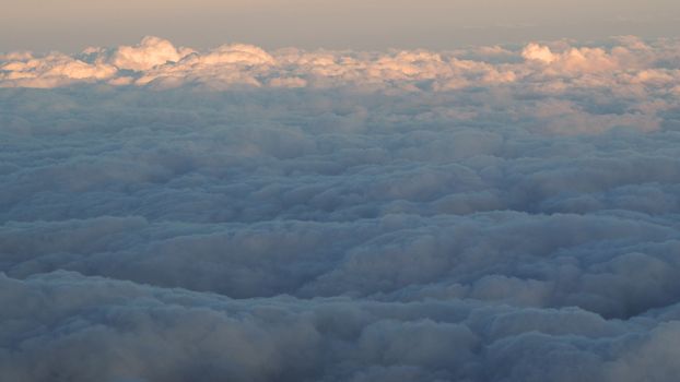 White clouds and blue sky with yellow warm sun light from airplane window.