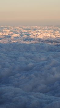 White clouds and blue sky with yellow warm sun light from airplane window.