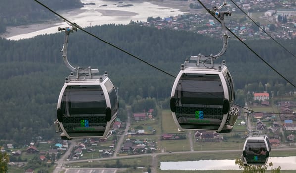 Manzherok resort, Altai Mountains, Russia - August 12, 2020: High angle shot of cableway with tourists inside cable cars on a cityscape background