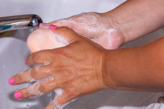 Close up shot of a woman lathering her hands with a soap bar using tap water. Pink finger nails. Hygiene concept.