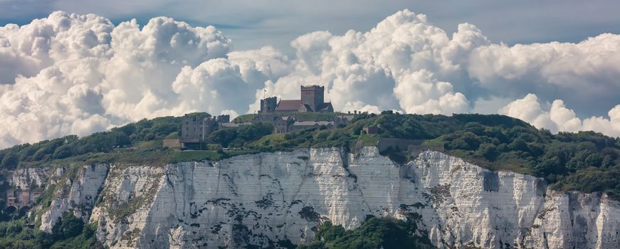 Panoramic shot of the White Cliffs of Dover and a castle on top of the cliff. Beautiful fluffy clouds in the background.