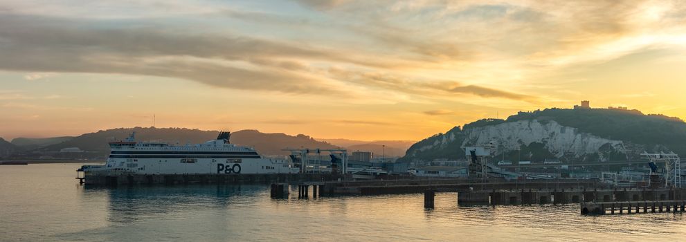 Port of Dover, England - June 24, 2020: Panoramic landscape shot of Dover Port with a P&O ferry boat docked at sunset. Beautiful warm orange sky and hills in the background.