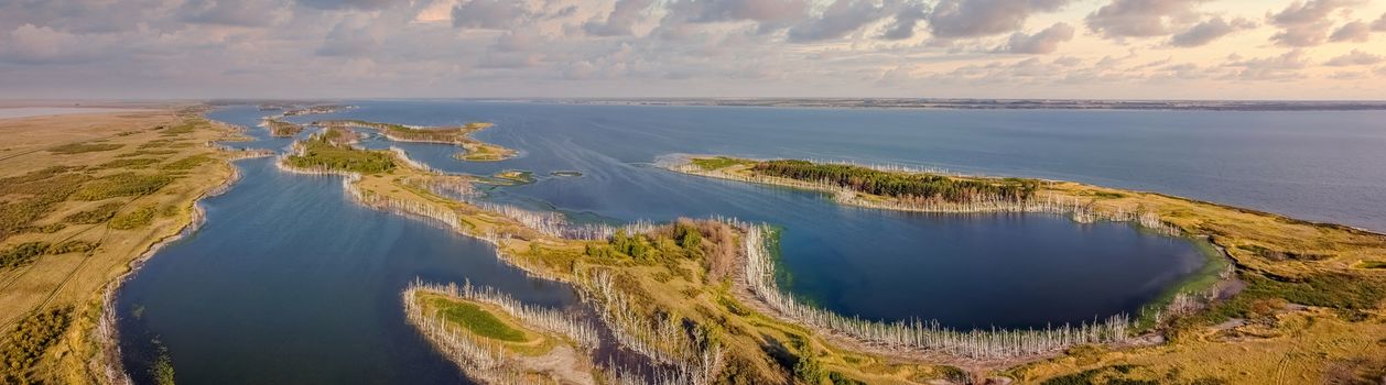 Beautiful panoramic high angle aerial drone shot of a cove and islands on one of Gorkoje lakes in Altai Krai, Siberia, Russia. Sunset cloudy sky in the background. Amazing landscape.