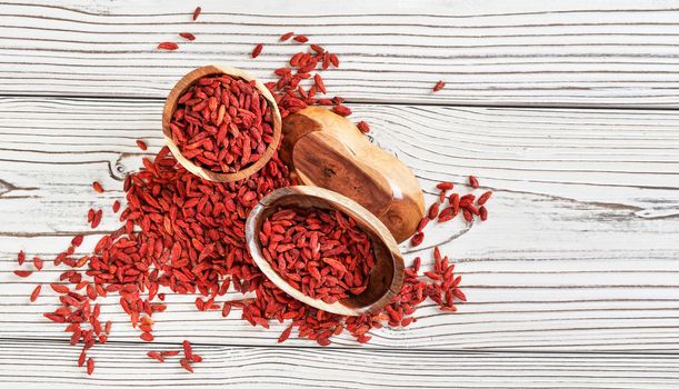 Dried goji berries in wooden bowls, scattered over white boards table under, view from above.