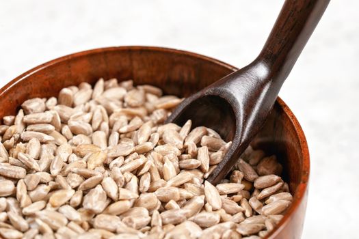 Peeled sunflower seeds in small wooden cup with little scoop, placed on white stone like board, closeup detail.