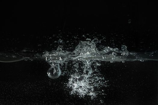 Water splashing as it's poured into aquarium tank, black background.