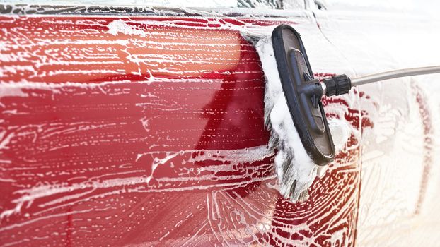 Red car washed in self serve carwash , detail on brush leaving strokes on side door, wide banner with empty space for text left side.