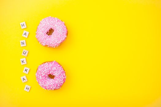 Bright pink delicious donuts on yellow background and inscription from wooden blocks happy hanukkah