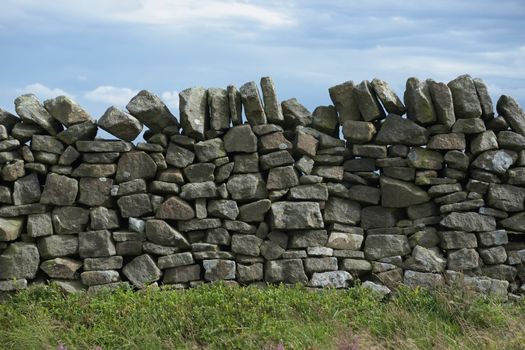 3 - Plain abstract background texture of dry stone wall. Close up of random mix of stone brickwork. Cloudy background and plants in foreground.
