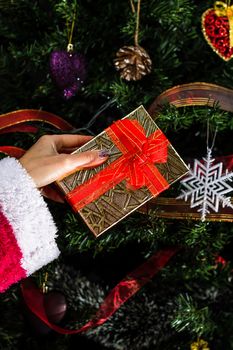 Hand holding present gift box in front of the Chhristmas tree.