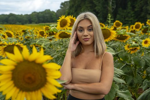 A gorgeous young blonde model poses outdoors in a field of sunflowers while enjoying a summers day