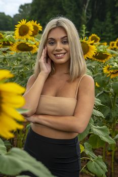 A gorgeous young blonde model poses outdoors in a field of sunflowers while enjoying a summers day