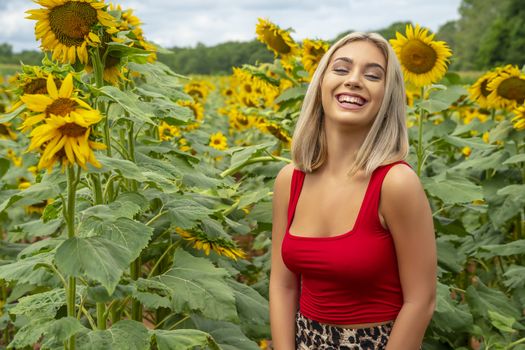 A gorgeous young blonde model poses outdoors in a field of sunflowers while enjoying a summers day