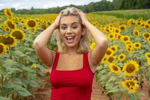 A gorgeous young blonde model poses outdoors in a field of sunflowers while enjoying a summers day
