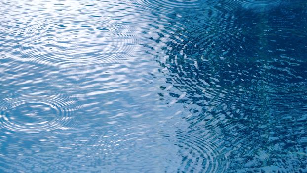 Rain drop falling on swiming pool and ripple shape and sun light reflection on water surface.