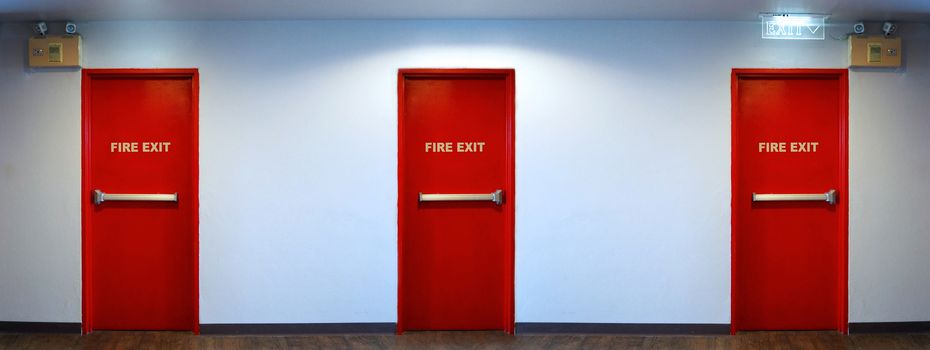 Emergency fire exit door red color metal material for safety protection and wood floor and white wall indoor building.