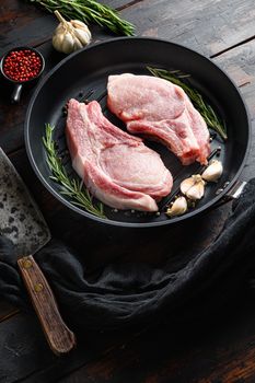 Raw pork pork rib roast in frying pan on a rustic wooden kitchen table with rosemary garlic peppercorns ingredients for grill and butcher knife side view selective focus..