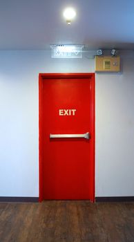 Emergency fire exit door red color metal material for safety protection and wood floor and white wall indoor building.