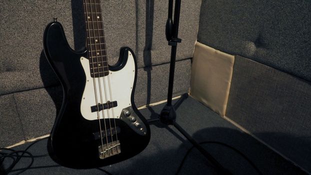 Bass guitar stand beside microphone tripod and absorb wall in the sound studio production.