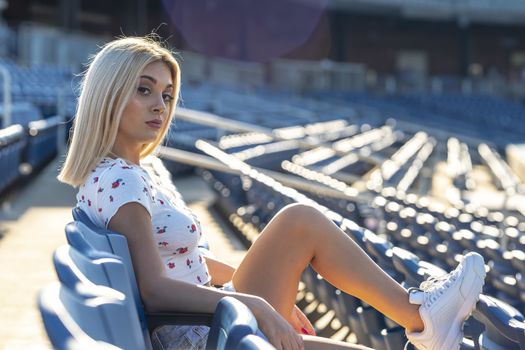 A gorgeous young blonde model poses outdoors while enjoying a summers day at a stadium before a game