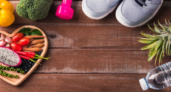 Top view of various fresh organic fruit and vegetable in heart plate and sports shoes, dumbbell and water, studio shot on wooden gym table, Healthy diet vegetarian food concept, World food day