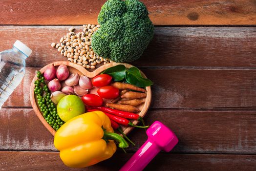 Top view of various fresh organic fruit and vegetable in heart plate and sports shoes, dumbbell and water, studio shot on wooden gym table, Healthy diet vegetarian food concept, World food day