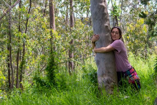 Real woman in hippie attitude hugging a tree in the middle of the forest. face mask