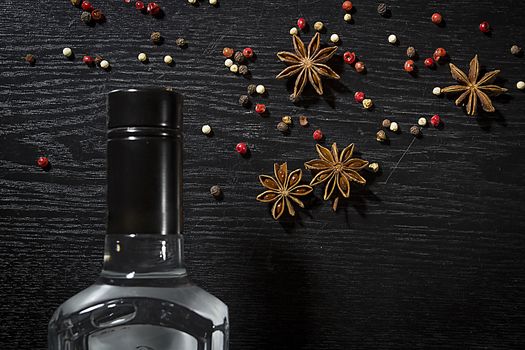 Bottle of anise vodka and spices on wooden black background