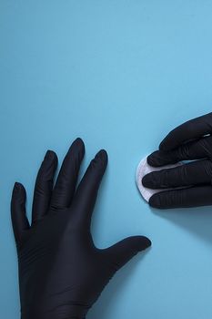 Hands in black nitrile gloves with a cotton sponge on a blue background