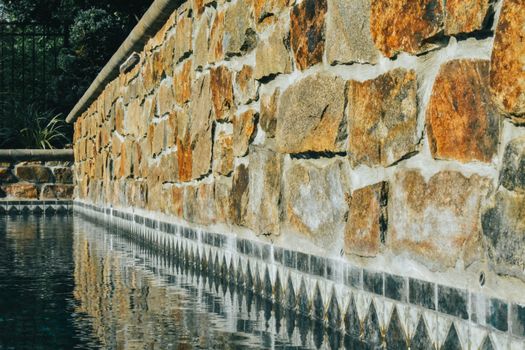 A Detailed Orange and Gray Cobblestone Wall Next to An In-Ground Pool