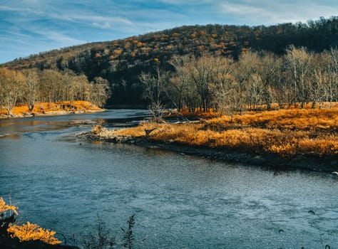 A Large Blue River Flowing Through an Orange Autumn Forest With a Mountain Behind It