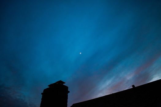 A Bright Blue and Purple Night Sky Over a Black Silhouetted Roof With a Chimney