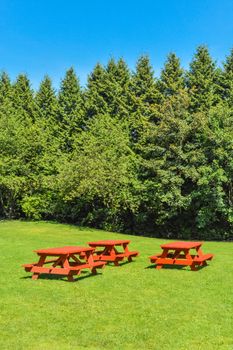 Rest area with red picnic tables on green lawn in a park