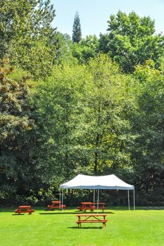 Rest area with red picnic tables and white tent installed on green lawn in a park