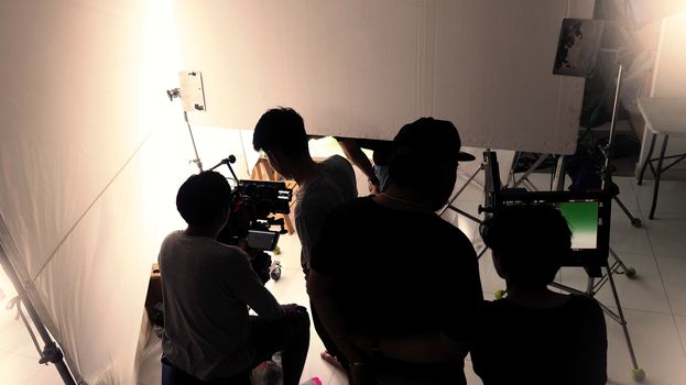 Behind the scenes of shooting video or movie production crew team and silhouette of camera and equipment in studio. 