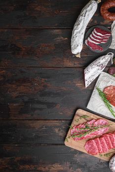 Variety of dry cured chorizo, fuet and other sausages cut in slices with herbs on old wooden table, flat lay with copy space.