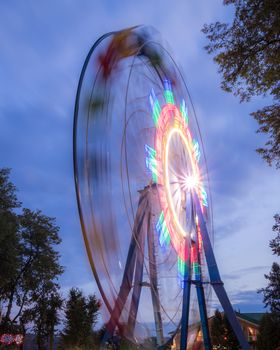 Rotating Ferris wheel in a night park with neon lighting against the sky.