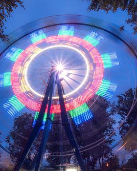 Rotating Ferris wheel in a night park with neon lighting against the sky.