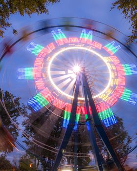 Rotating Ferris wheel in a night park with neon lighting against the sky.